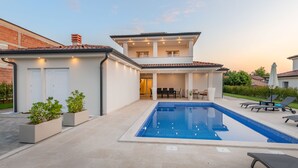 A modern two-story house with a swimming pool, outdoor seating, and a brick wall.
