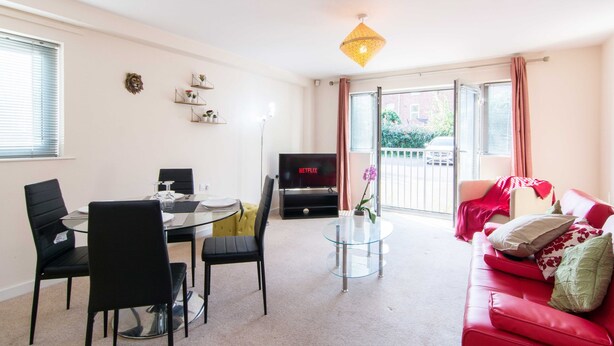 Un salón con una mesa de comedor de cristal, sillas negras, un sofá rojo, un televisor y un balcón con vistas.