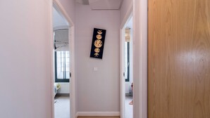 Un couloir doté d’un plancher en bois, une œuvre d’art noire accrochée au mur et une vue sur une pièce avec une fenêtre et un radiateur.