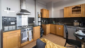 Une cuisine compacte avec des meubles en bois, une cuisinière à gaz, une hotte en acier inoxydable et un dosseret de carrelage noir.
