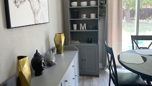 Ein Essbereich mit Tisch, Stühlen, einer Kommode mit Dekorationsobjekten und einem gerahmten Kunstwerk an der Wand.