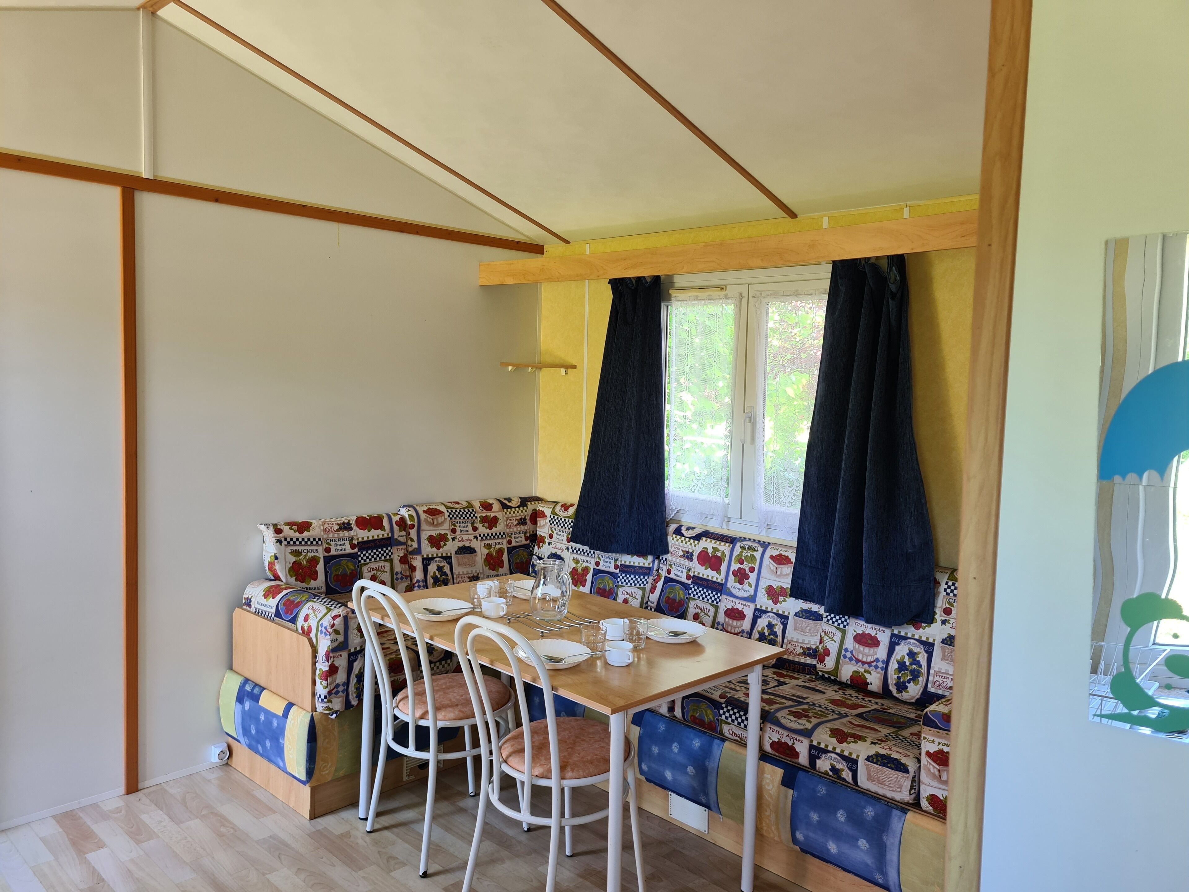 A cozy dining area with a wooden table, white chairs, and a bench with a colorful fabric.