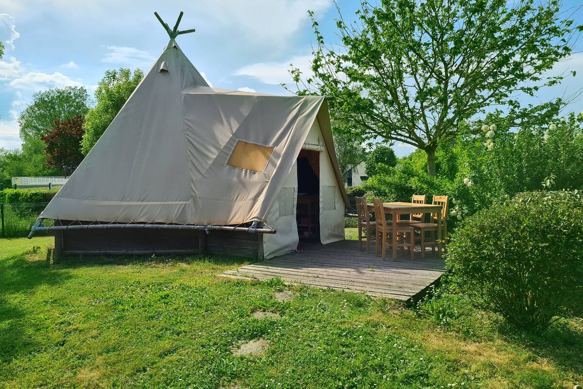 A white tent with a teepee entrance, a wooden table, and chairs outside.