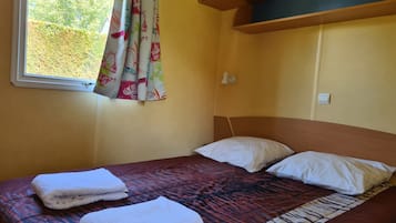 Ein Zimmer mit einem Bett, zwei Kissen, einem Fenster mit Vorhängen, einer Wandleuchte und einem Thermostat.