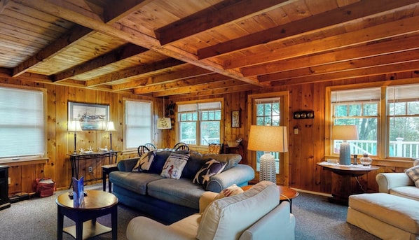 L’intérieur d’un chalet accueillant, avec un plafond en bois, un canapé, une table à manger et une fenêtre donnant sur les arbres.