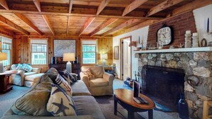 A cozy cabin interior with a stone fireplace, wooden beams, and a comfortable seating area. - All Aboard Cottage (East Boothbay)