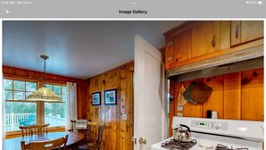 A wooden interior with a dining area featuring a table and chairs, a kitchen with a stove, and wooden walls. - All Aboard Cottage (East Boothbay)