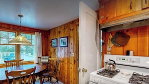 Un intérieur en bois comprenant un coin repas avec une table et des chaises, une cuisine équipée d’une cuisinière et des murs en bois.