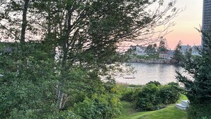 A grassy area with a body of water, trees, and a distant building. - All Aboard Cottage (East Boothbay)