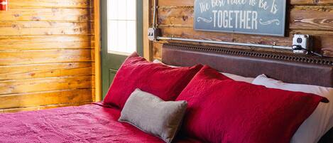 A cozy room with a wooden wall, a bed with red and grey pillows, and a sign that says "The Best Place To Be Is Together".