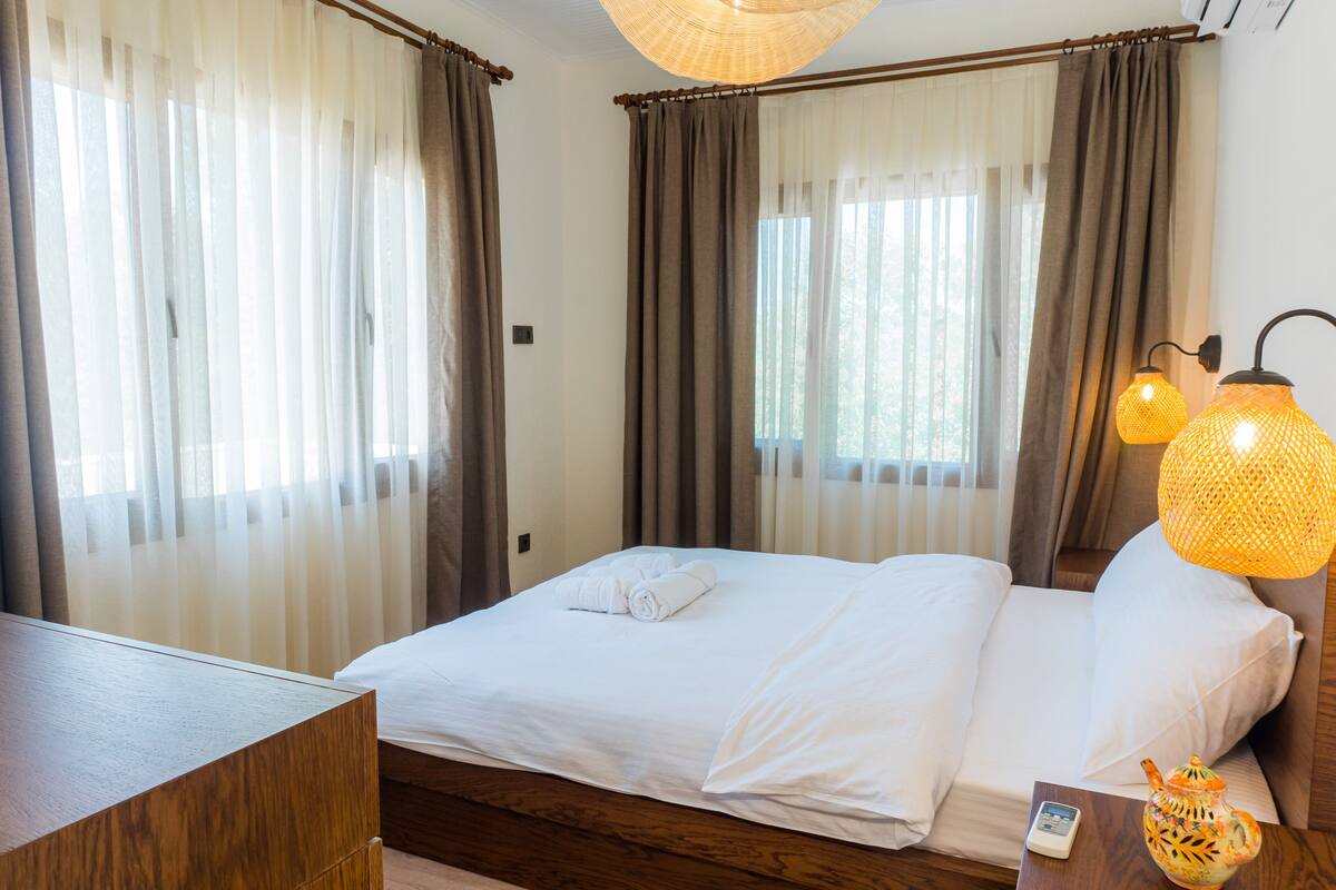 Una cama bien hecha con sábanas blancas, una mesita de noche de madera y una lámpara decorativa.