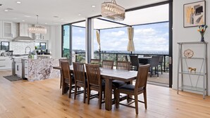 A modern kitchen with white cabinetry, a marble island, and a dining area with wooden chairs and a table. - 360° HILLTOP VIEW / Ultra Modern / 15min DISNEY (Santa Ana)