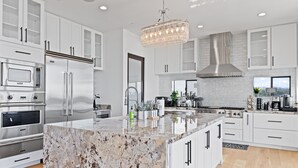 A modern kitchen with white cabinetry, a large marble island, stainless steel appliances, and a chandelier. - 360° HILLTOP VIEW / Ultra Modern / 15min DISNEY (Santa Ana)