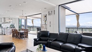 A spacious living area with a black leather sofa, a dining table with chairs, and a kitchen in the background. - 360° HILLTOP VIEW / Ultra Modern / 15min DISNEY (Santa Ana)