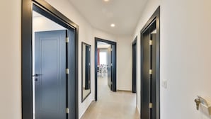 Un pasillo con varias puertas, suelo de baldosas y vista a un comedor.