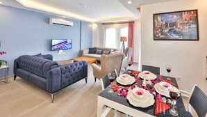 Una sala de estar moderna con un sofá, una mesa de comedor preparada para dos personas y un televisor de pantalla plana montado en la pared.