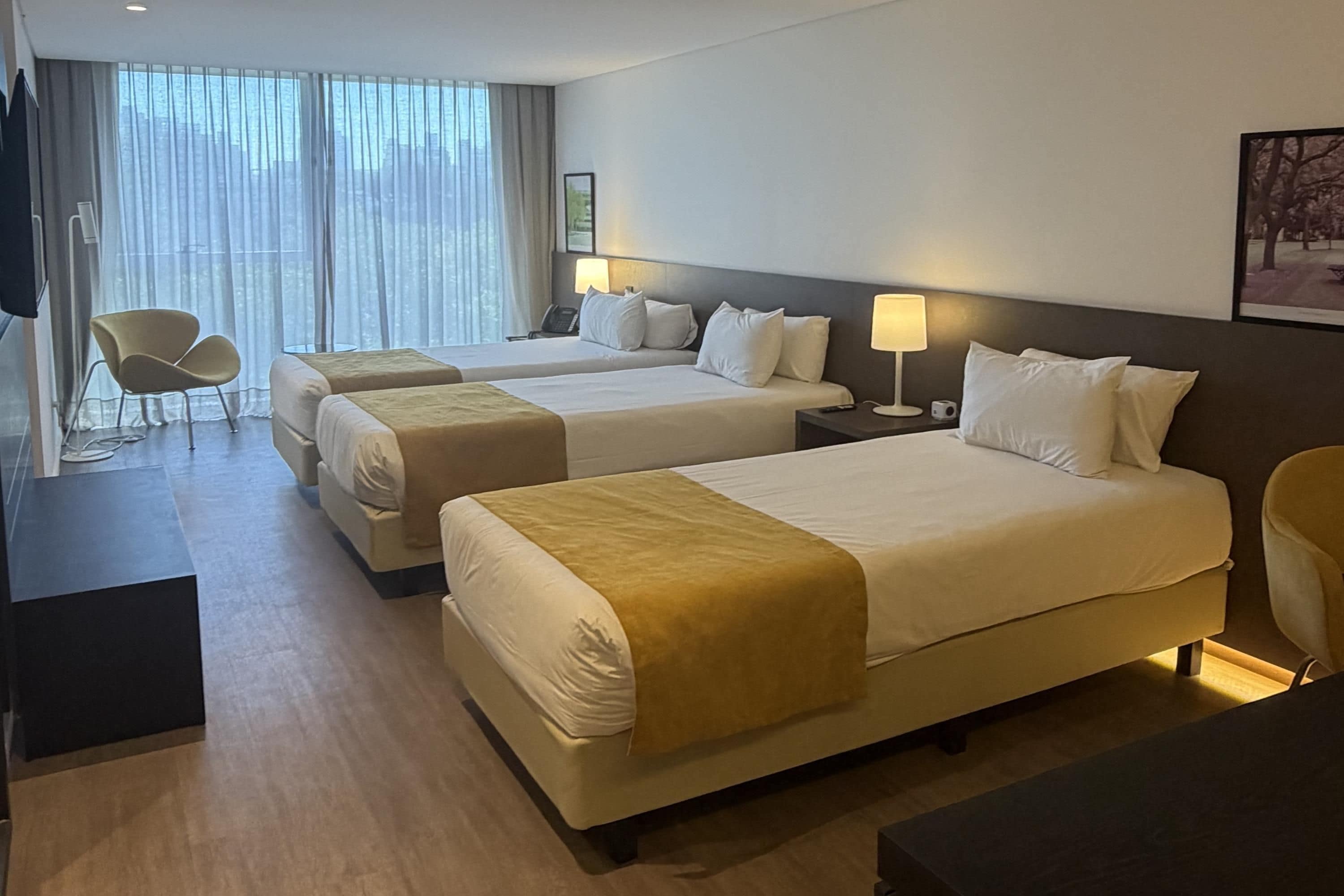 A hotel room with two beds, a desk, a chair, a lamp, and a window with curtains.