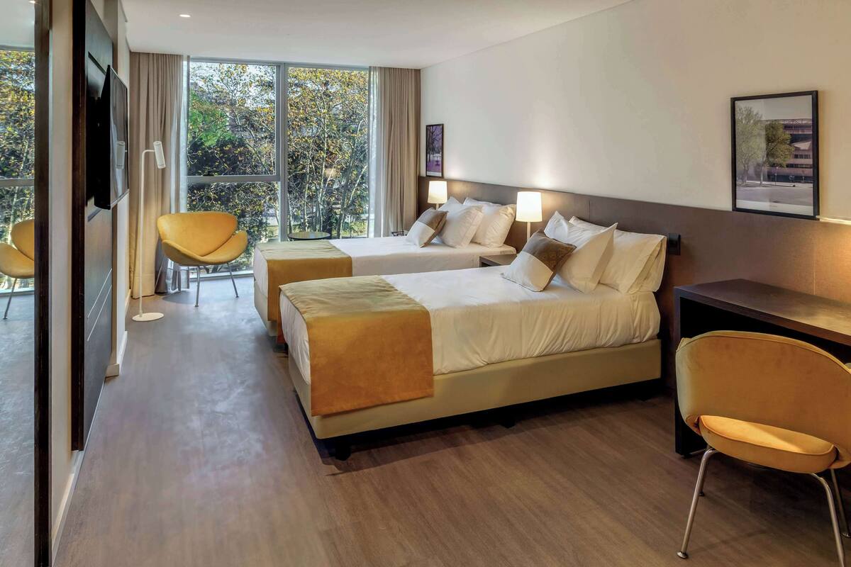 A hotel room with two beds, a TV, a desk, and a chair.