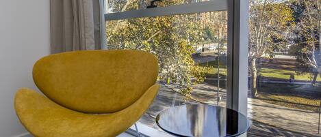 Una habitación moderna con un ventanal grande, una silla amarilla y una mesita redonda.