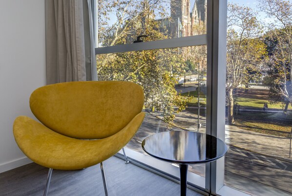 Una habitación moderna con un ventanal grande, una silla amarilla y una mesita redonda.