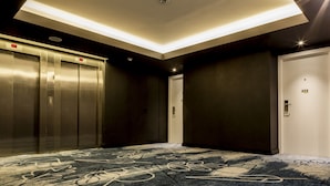 A modern elevator area with a patterned carpet, a ceiling light fixture, and a door marked with the number 205.