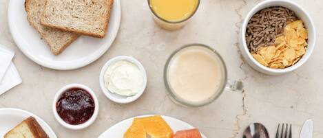 A breakfast setting with toast, orange slices, grapefruit, cereal, and a glass of orange juice.