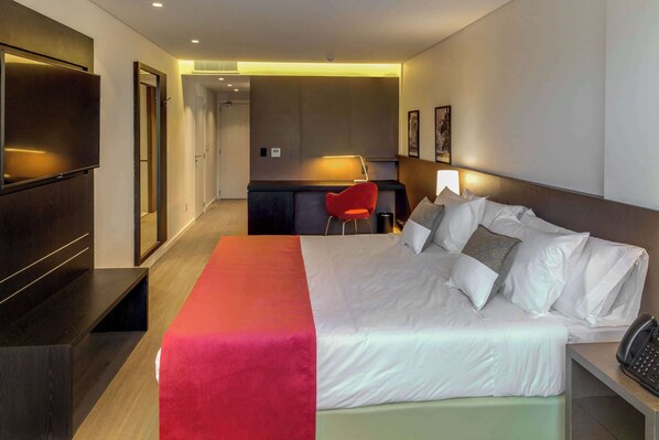 A hotel room with a bed, bedside table, and a desk with a chair.