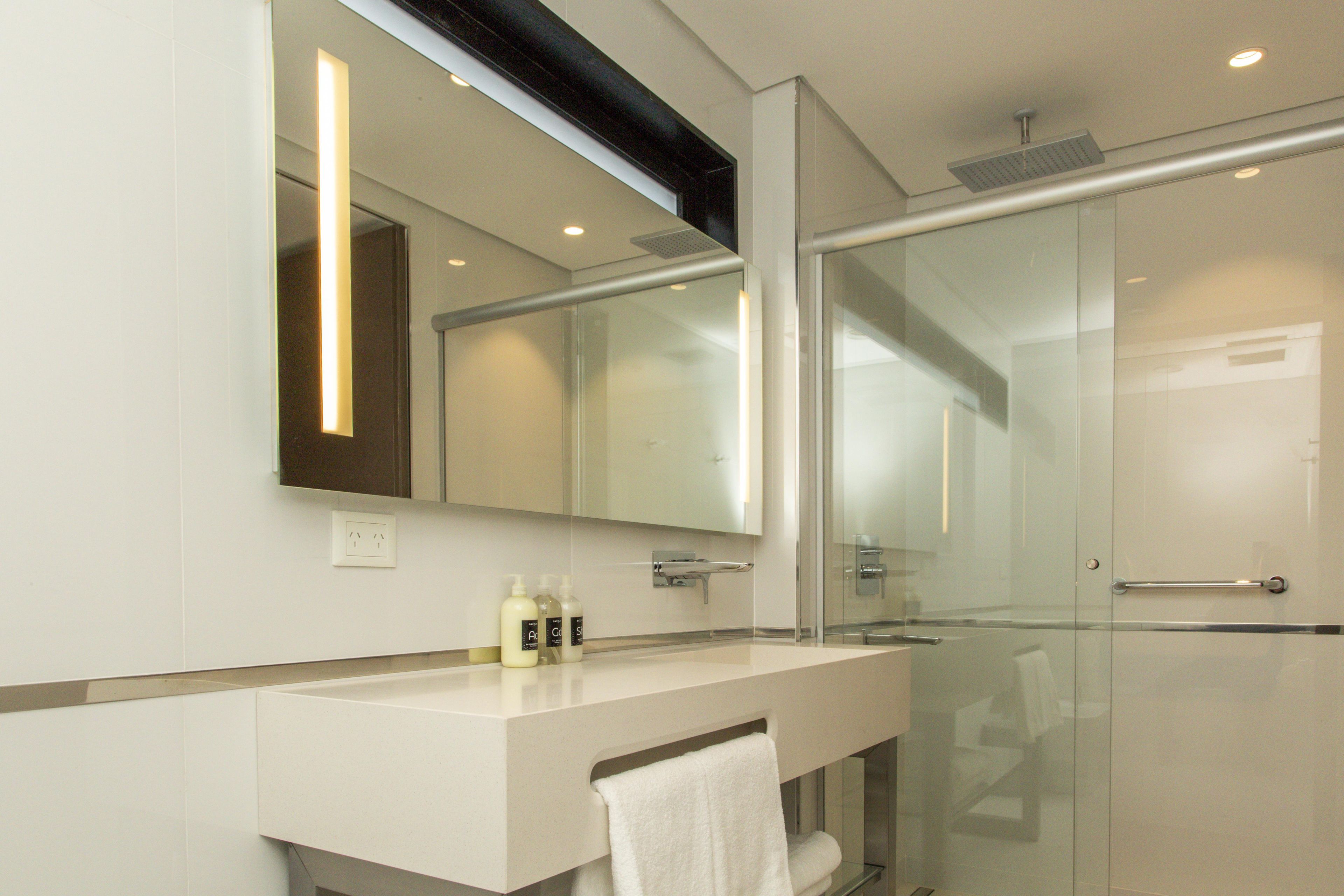 Un baño moderno con cabina de ducha de vidrio, tocador blanco y un espejo grande.
