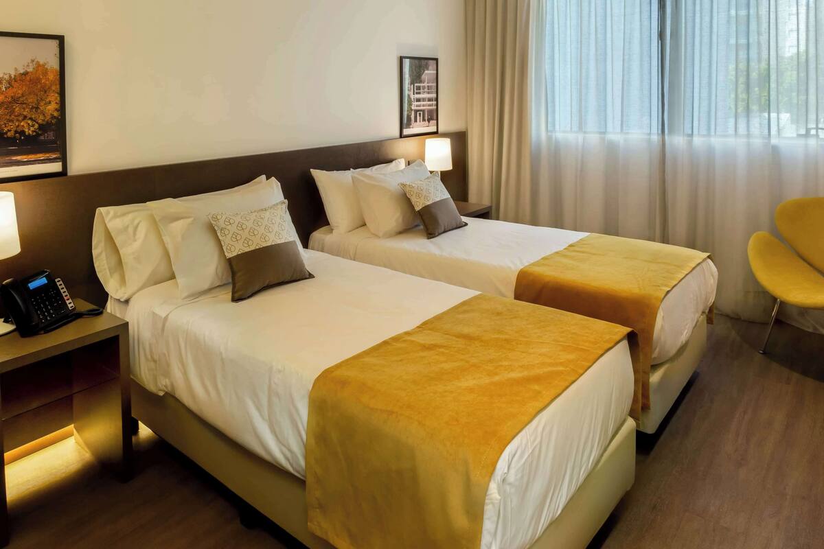 A hotel room with two beds, a bedside phone, and a chair.