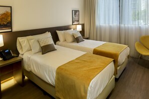 Una habitación de hotel con dos camas, una mesita de noche con teléfono, una silla y una ventana con cortinas.