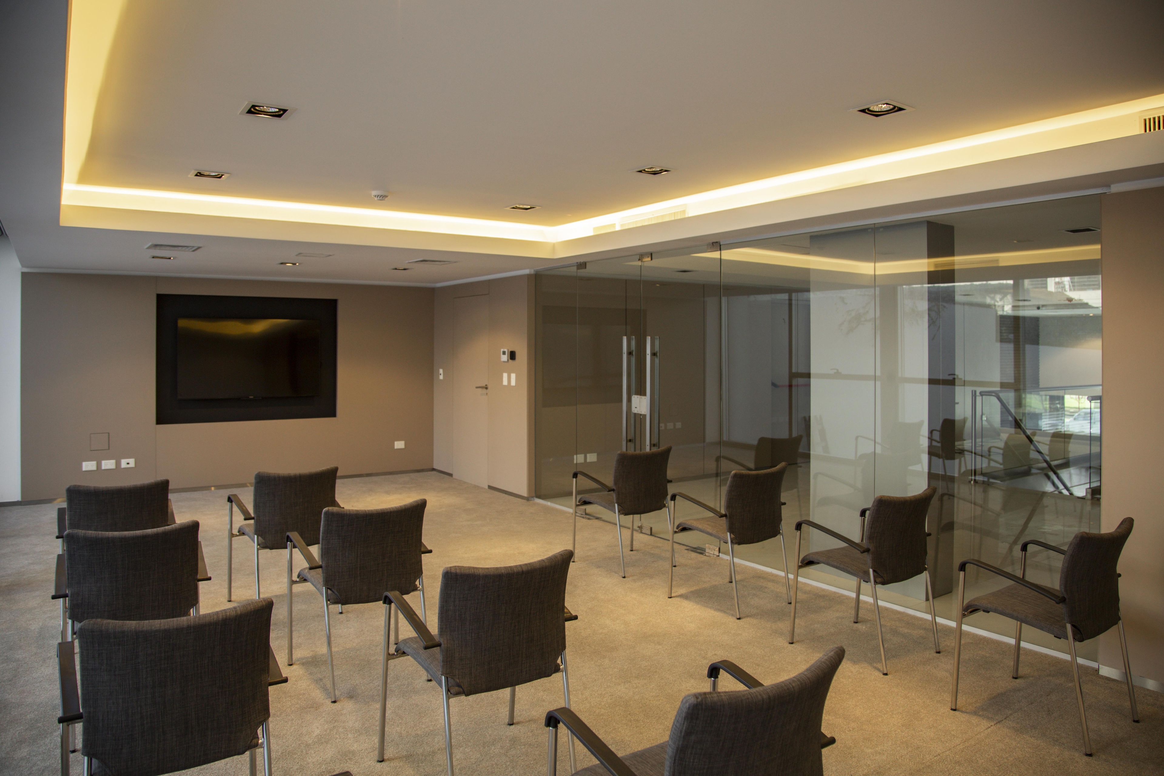 Ein Konferenzraum mit modernem Design, der eine Glastrennwand, mehrere Stühle, einen Flachbildfernseher und deckenintegrierte Beleuchtung umfasst.