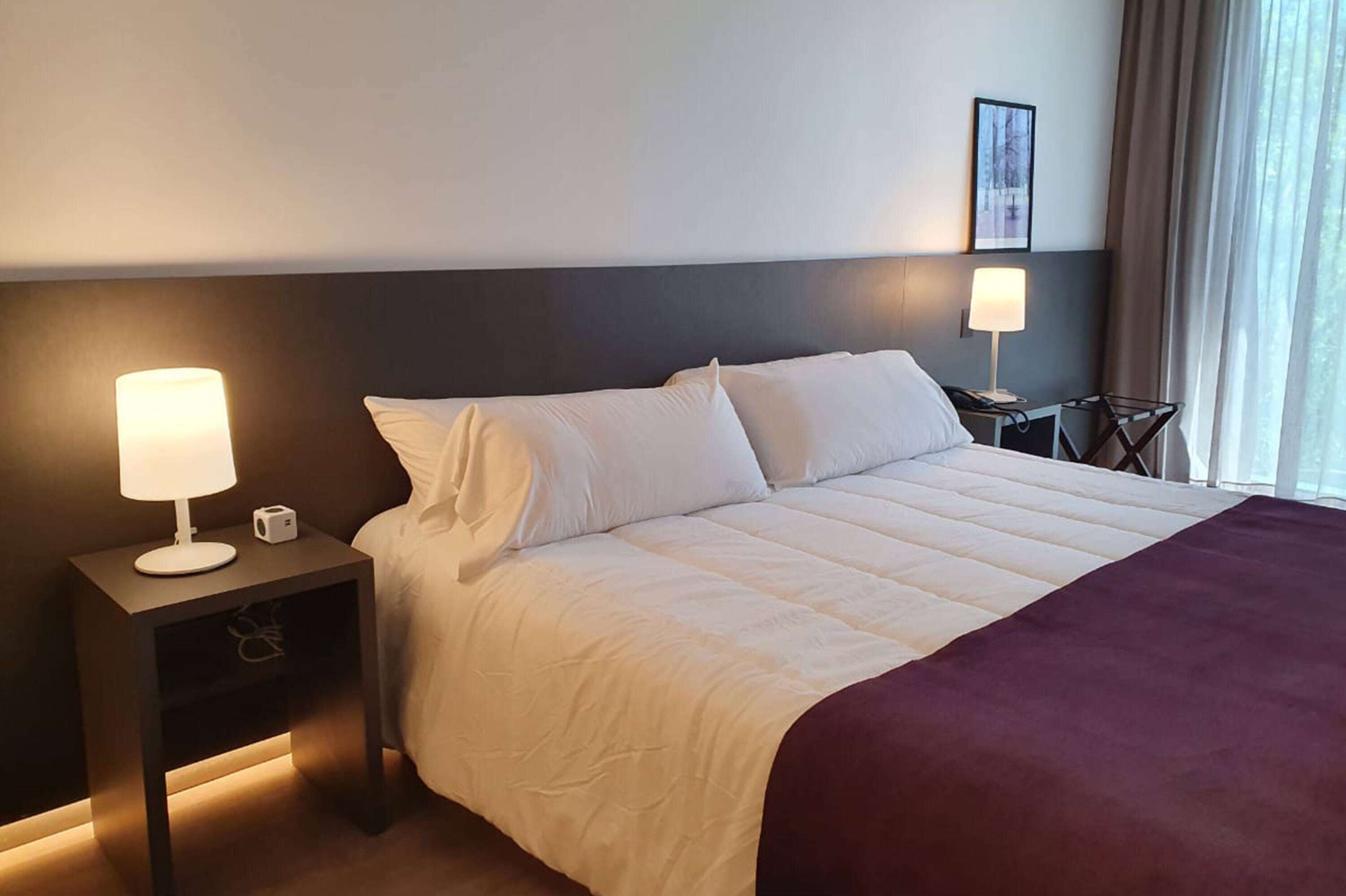 Ein Hotelzimmer mit einem großen Bett, zwei Nachttischen, einer Lampe und einem gerahmten Bild an der Wand.