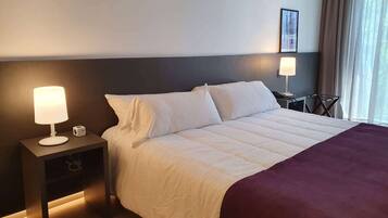 A hotel room with a large bed, two bedside tables, a nightstand, a lamp, and a framed picture on the wall.