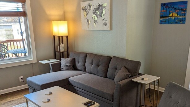 Un salon avec un canapé gris, une table basse, une table d’appoint, une lampe et un ventilateur de plafond.