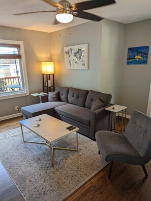 Relax in this stylish living room with a grey sofa, coffee table, and armchair, surrounded by wall art and a ceiling fan.