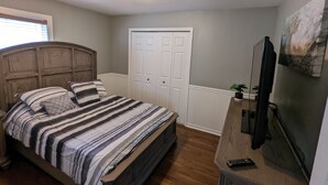 Une chambre à coucher avec un lit, une commode, un téléviseur et une porte.