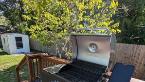 Un barbecue sur une terrasse en bois, avec une clôture en bois et un abri de jardin en arrière-plan.