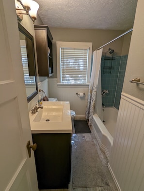 Bathroom features a sink, vanity, and mirror, with a shower area and window with blinds.
