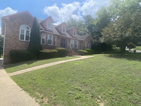 A two-story brick house with a well-maintained lawn, a pathway leading to the front door, and a large tree to the right.