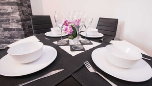 A dining table set with white plates, bowls, cutlery, and wine glasses, with a vase of purple flowers in the center. - Michaelmas, Coventry - 2 Bed House Apartment (Coventry)