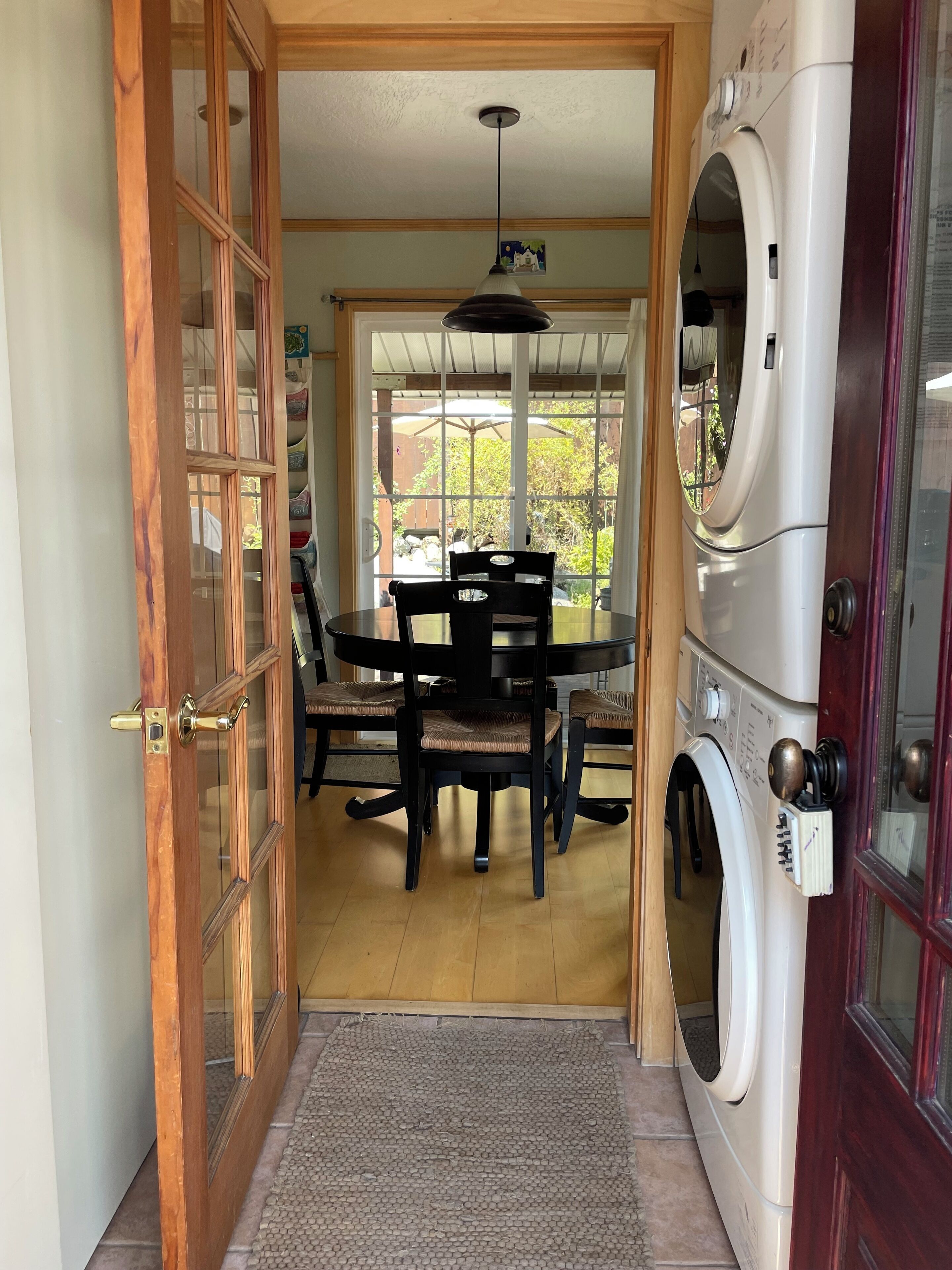 Une pièce avec une porte en bois, une table à manger avec des chaises, un lave-linge et une vue sur l’extérieur.