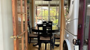 Una habitación con puerta de madera, una mesa de comedor con sillas, una lavadora y vistas al exterior.