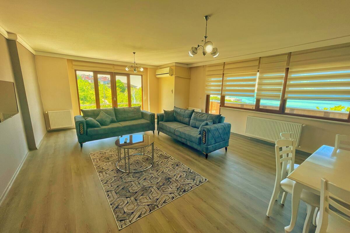 A spacious living room with a large sofa, a dining table, and a ceiling fan.