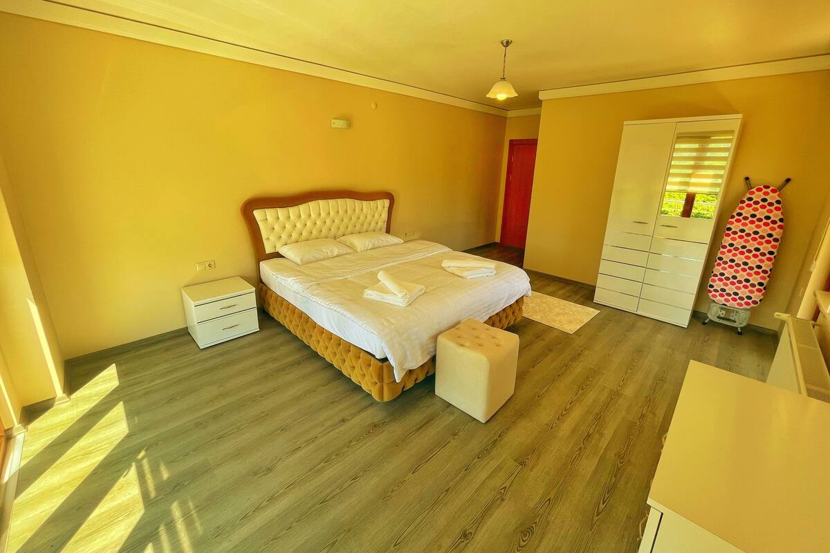 A bedroom with a bed, a wardrobe, a small bedside table, and a large mirror.