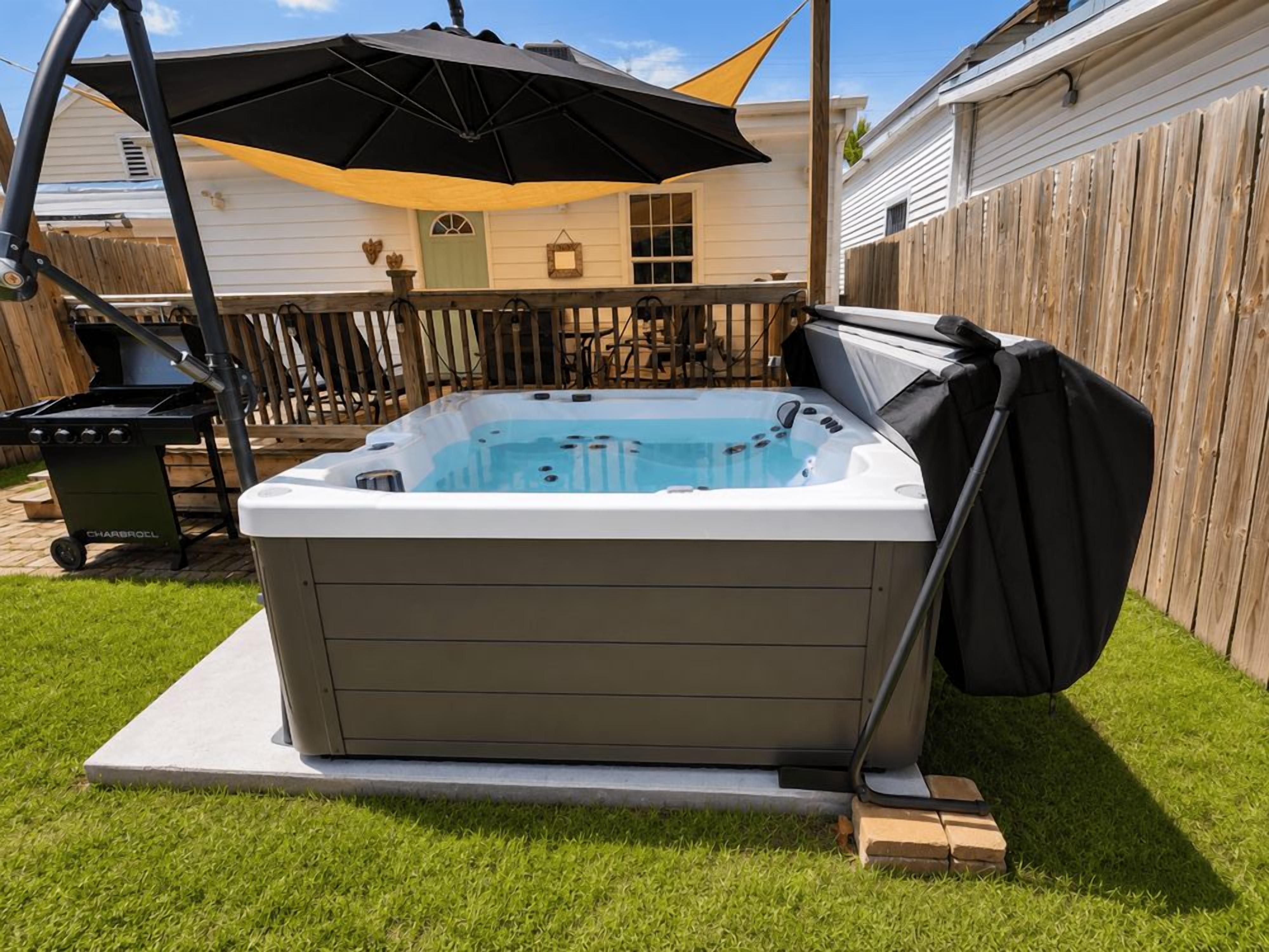 A hot tub in a backyard with a covered patio area and a wooden fence.