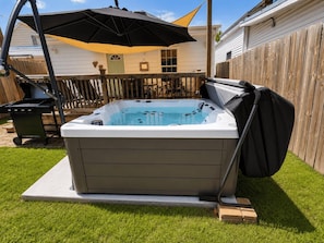 A hot tub in a backyard with a covered patio area and a wooden fence.