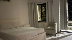Een slaapkamer met een bed, een stoel, een nachtkastje en een raam met gordijnen.