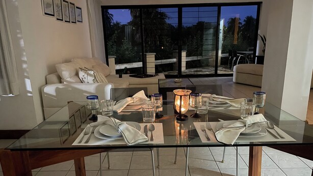 Een eethoek met een glazen tafel voor vier personen, omringd door een moderne zithoek met een bank en uitzicht op het omliggende landschap.