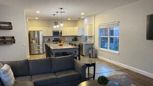 A modern kitchen with a central island, a dining area, and a living room with a sofa and a coffee table.