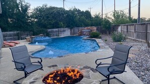 A backyard with a swimming pool, a fire pit, and two chairs.